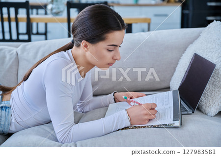 Young student girl study online, lying at home on couch with laptop, notebook 127983581