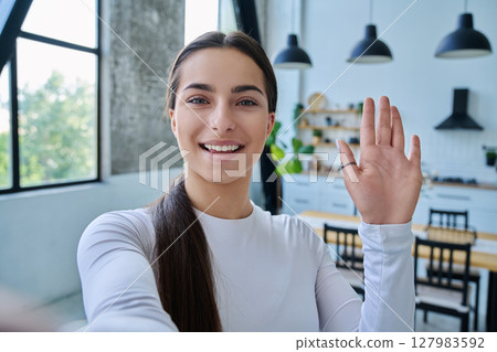 Close-up selfie portrait of teenage female looking waving hand at web camera 127983592