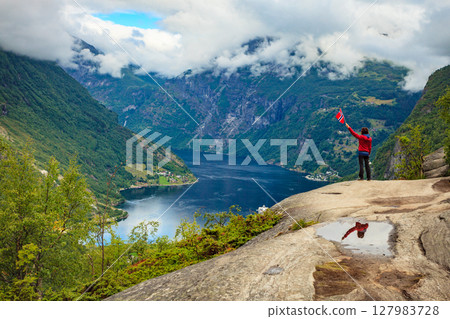 Tourist over Geirangerfjord holds norwegian flag Tourist over Geirangerfjord holds norwegian flag 127983728