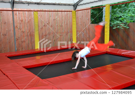 Happy girl having fun while jumping on trampoline. Sports girl jumps on a trampoline. Outdoor shot of girl jumping on trampoline, enjoys jumping in home. happy summer vacation. High quality photo Happy girl having fun while jumping on trampoline. Sports girl jumps on a trampoline. Outdoor shot of girl jumping on trampoline, enjoys jumping in home. happy summer vacation. High quality photo 127984095