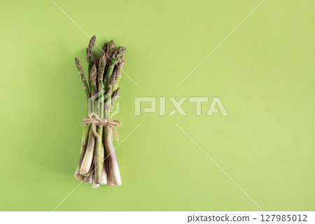 Fresh asparagus tied bundle on vibrant green background. Top view Fresh asparagus tied bundle on vibrant green background. Top view 127985012