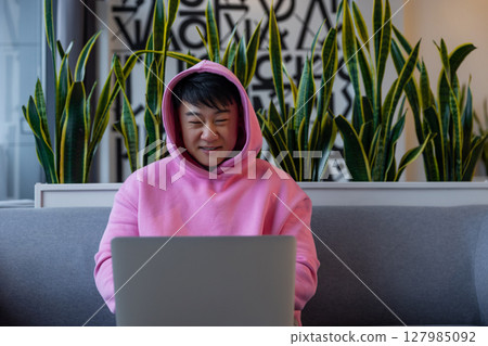 Asian young man in a pink hoodie at the laptop 127985092