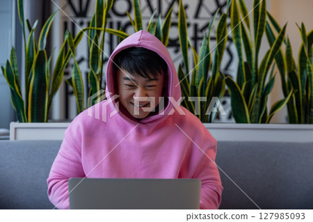 Asian young man in a pink hoodie at the laptop Asian young man in a pink hoodie at the laptop 127985093