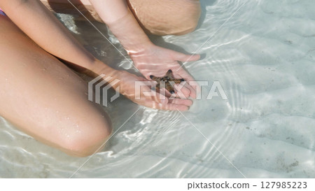 Girl holds starfish in ocean water at tropical beach 127985223