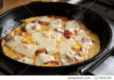 scrambled eggs with tomatoes and pieces of hard cheese in a frying pan on a gas stove 127985240