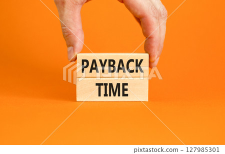 Payback time symbol. Concept words Payback time on wooden blocks. Beautiful orange table orange background. Businessman hand. Business and payback time concept. Copy space. 127985301