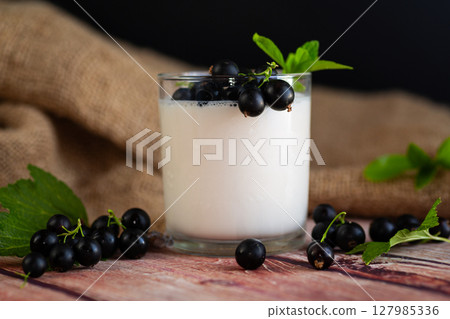 Blackcurrant and homemade yogurt in a transparent glass on a wooden 127985336