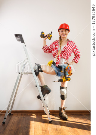 Woman wearing helmet, toolbelt on ladder Woman wearing helmet, toolbelt on ladder 127985649