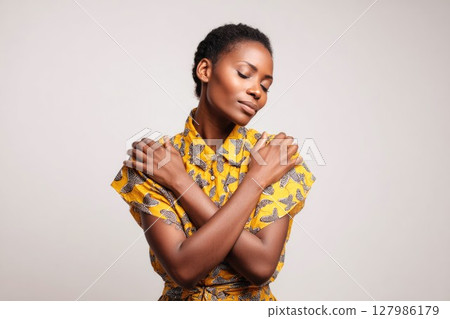 Young female touching and tapping her shoulders, crossing hands. Psychology and self-care concept, butterfly hug, African woman hugging herself on a light background 127986179