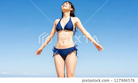 A woman in a bikini with her arms outstretched against the blue sky 127986576