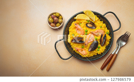Spanish seafood Paella with shrimps, mussels, peas and lemon in a pan on light beige background top view 127986579