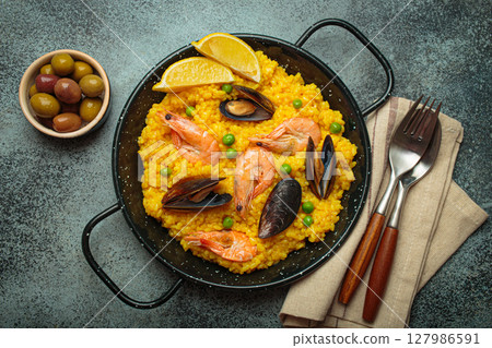 Spanish seafood Paella with shrimps, mussels, peas and lemon in a pan on dark rustic background top view Spanish seafood Paella with shrimps, mussels, peas and lemon in a pan on dark rustic background top view 127986591