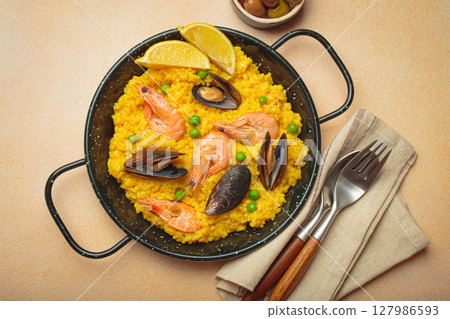 Spanish seafood Paella with shrimps, mussels, peas and lemon in a pan on light beige background top view Spanish seafood Paella with shrimps, mussels, peas and lemon in a pan on light beige background top view 127986593