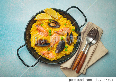 Spanish seafood Paella with shrimps, mussels, peas and lemon in a pan on light blue background top view. Mediterranean meal 127986594