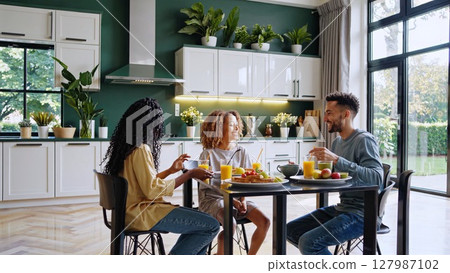 Diverse family sharing morning meal, laughing and connecting while preparing breakfast in contemporary kitchen, experiencing warmth of familial togetherness 127987102