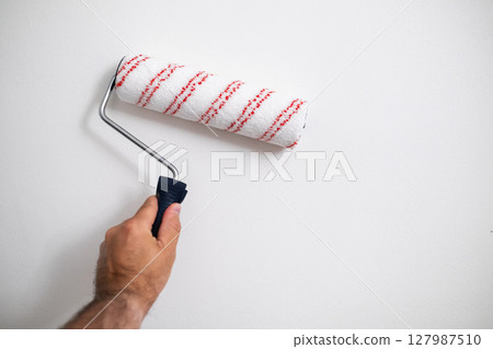 Strong male hand holding a roller, painting a wall indoors, concept of DIY home improvement Strong male hand holding a roller, painting a wall indoors, concept of DIY home improvement 127987510