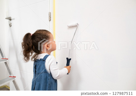 Cute girl painting the wall in a stylish living room, helping with apartment makeover. 127987511