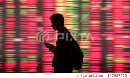 Silhouette of a man walking in front of a stock ticker board 127987710