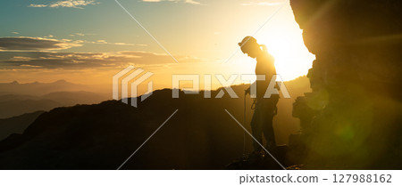 Young girl is preparing for training on the rocks sunset, in the mountains and puts a helmet 127988162