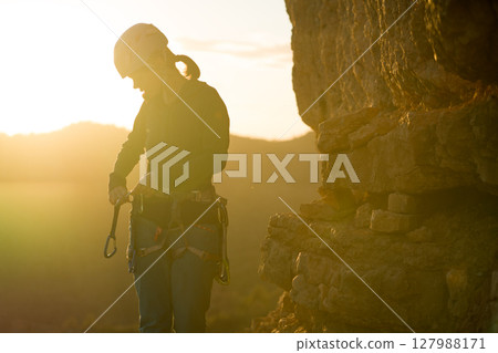 Young girl is preparing for training on the rocks sunset, in the mountains and puts a helmet Young girl is preparing for training on the rocks sunset, in the mountains and puts a helmet 127988171