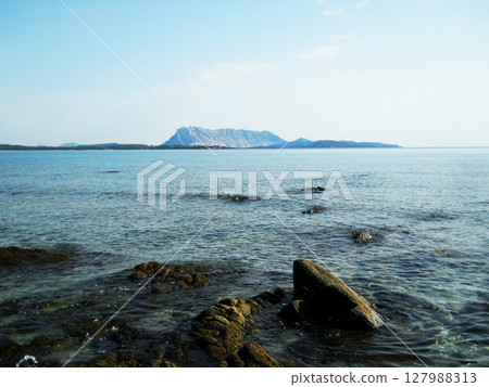 Beautiful sea view featuring the majestic Tavolara Island off the coast of Sardinia, Italy. The crystal-clear turquoise waters of the Mediterranean Sea stretch toward the horizon, with the dramatic 127988313