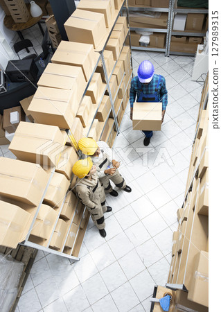 Multiethnic staff in safety gear managing merchandise and logistics operations. Warehouse environment designed for effective inventory and transportation, distribution management. 127989315