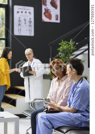 Nurse assisting asian patient in measuring her sugar levels with glucometer for a routine checkup in waiting room. Specialist explains diabetes reading interpretation for glucose levels. 127989391