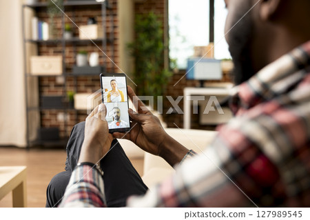 Self employed black man using cellphone for virtual meeting with potential investors. African american entrepreneur on video call, seeking financial advice from team of caucasian accountants. Self employed black man using cellphone for virtual meeting with potential investors. African american entrepreneur on video call, seeking financial advice from team of caucasian accountants. 127989545