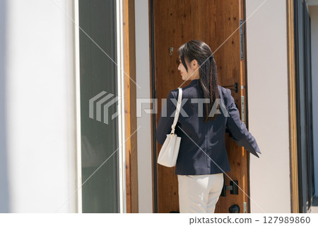 A woman in a suit opening the front door 127989860