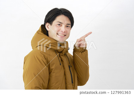 一名身穿羽絨外套的男子指向白色背景的右側 127991363