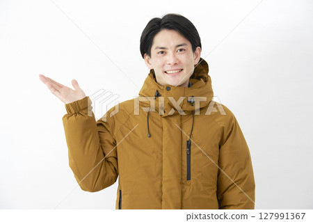 一名身穿羽絨外套的男子用手掌指向白色背景下的左側 127991367
