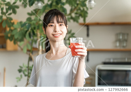 Young Asian woman drinking tomato juice, acerola, BCAA, red drink in front of her kitchen 127992666