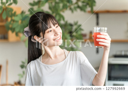 年輕的亞洲女性在廚房前喝番茄汁、西印度櫻桃、支鏈胺基酸和紅飲料 年輕的亞洲女性在廚房前喝番茄汁、西印度櫻桃、支鏈胺基酸和紅飲料 127992669