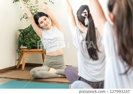 A female yoga teacher/instructor teaching yoga and pilates in a yoga class and a female student A female yoga teacher/instructor teaching yoga and pilates in a yoga class and a female student 127993287