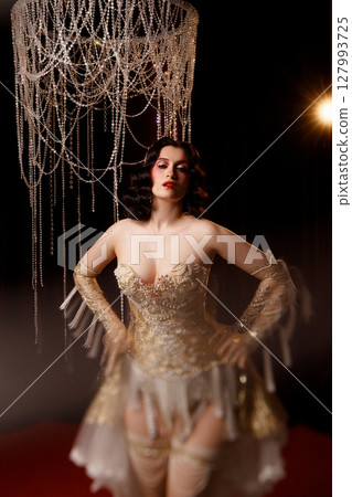 Circus show performer in vintage corset costume under chandelier on dark background 127993725