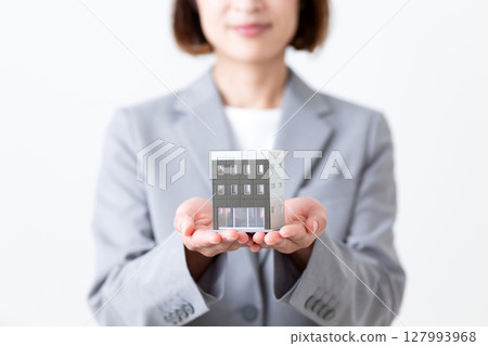 A middle-aged woman in a gray suit holding a model of a building A middle-aged woman in a gray suit holding a model of a building 127993968