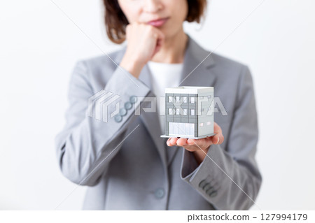 一位身穿灰色西裝的中年婦女擔心一棟建築的房屋模型 一位身穿灰色西裝的中年婦女擔心一棟建築的房屋模型 127994179