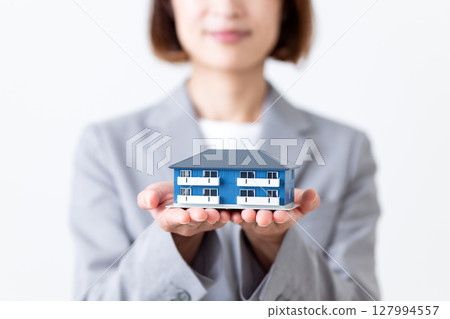 A middle-aged woman in a gray suit holding a model of an apartment house 127994557