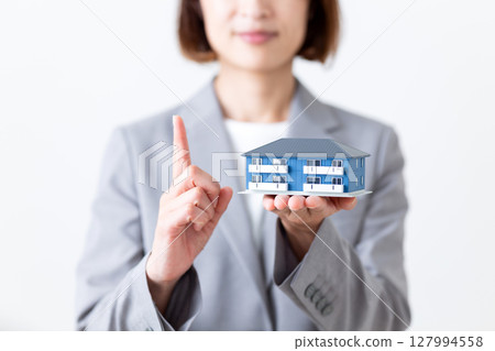 一位身穿灰色西裝的中年婦女手裡拿著一棟公寓大樓的模型，食指向上 127994558