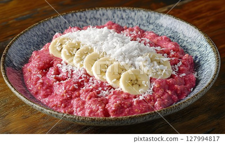 Vibrant pink porridge bowl with banana and coconut topping 127994817