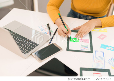 User Interface Designer Asian Woman Creating Mobile App Design on Tablet with Laptop and Devices for Website and Application Ideas 127994822