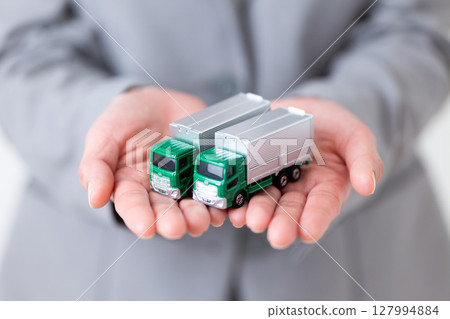 一位身穿灰色西裝的中年婦女手裡拿著一輛卡車的模型 127994884