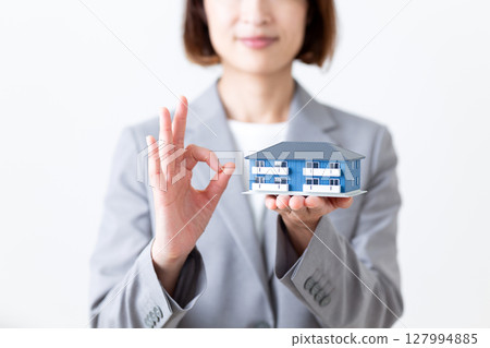 一位身穿灰色西裝的中年女子手持公寓模型，擺出一個圓圓的姿勢 127994885