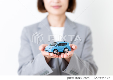 A middle-aged woman in a gray suit holding a model car A middle-aged woman in a gray suit holding a model car 127995476