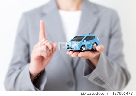 一位身穿灰色西裝的中年婦女，手裡拿著一輛模型車，食指向上 127995478