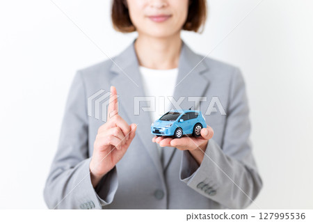 一位身穿灰色西裝的中年婦女，手裡拿著一輛模型車，食指向上 127995536
