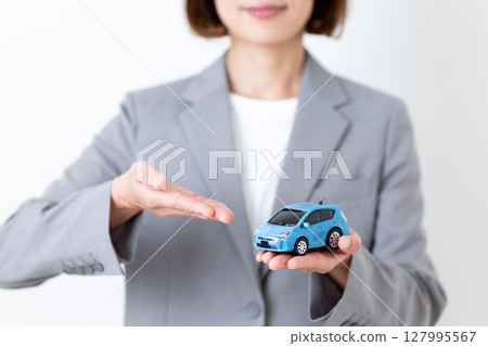 A middle-aged woman in a gray suit holding a model car and recommending it A middle-aged woman in a gray suit holding a model car and recommending it 127995567