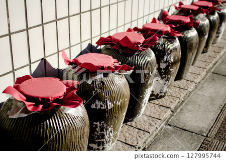 A scene of many pottery pieces with red lids lined up in front of a building and road A scene of many pottery pieces with red lids lined up in front of a building and road 127995744