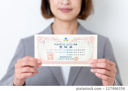 A middle-aged woman in a gray suit holding a stock certificate 127996356