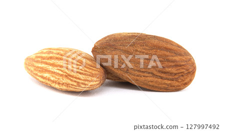 A close-up image features three almonds on a clean white background, emphasizing their texture. A close-up image features three almonds on a clean white background, emphasizing their texture. 127997492